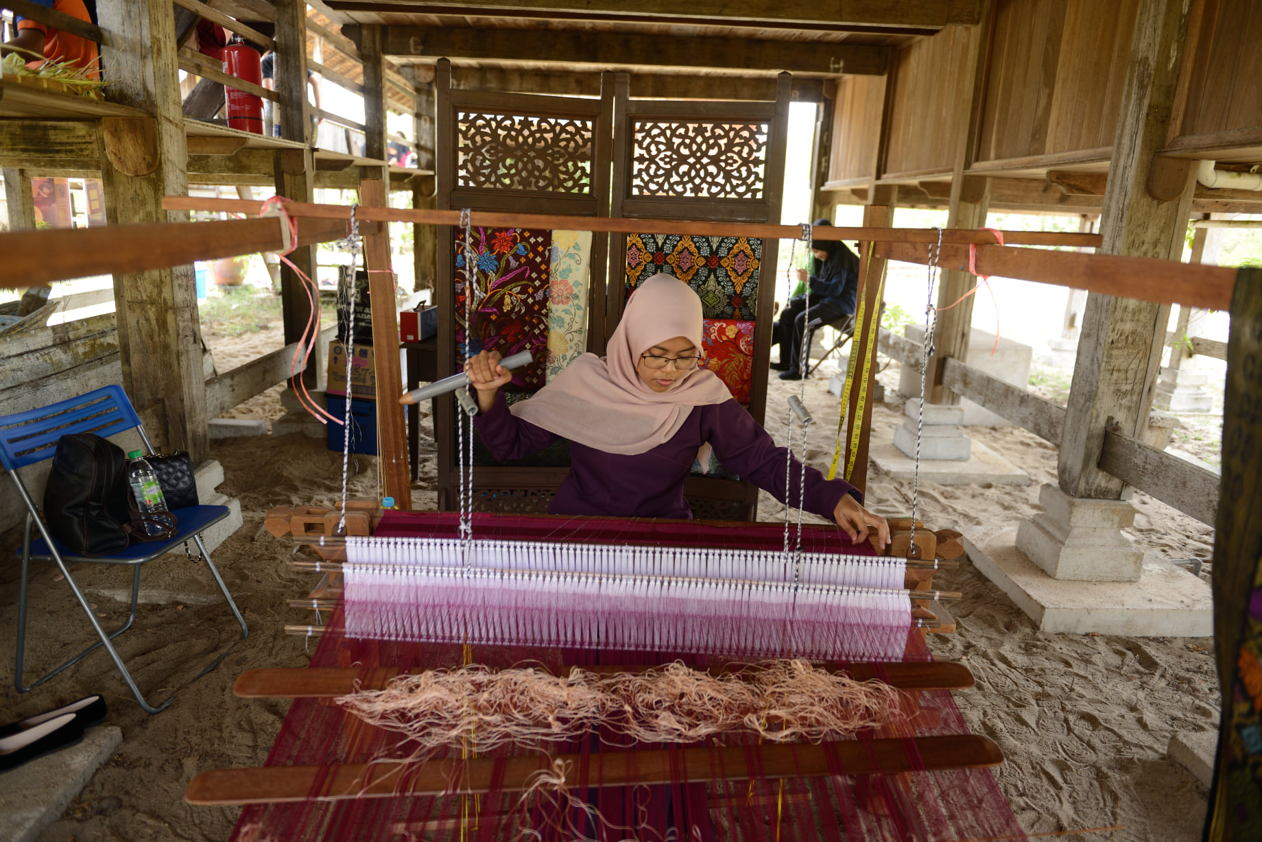 Efa, a weaver, pulls threads through a wooden loom to create textiles, a craft that Terrapuri showcases and supports by offering them for sale on its online store, Terradala. Photo courtesy of Terrapuri Heritage Village