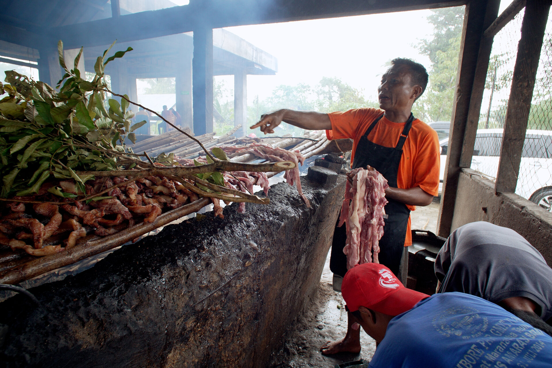 A cook at the Se’i Baun smokehouse puts fresh pork on the smoking furnace while directing the junior staff.